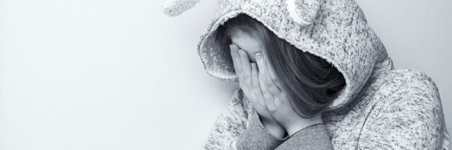 A girl wearing a hoodie covering her face with both hands.