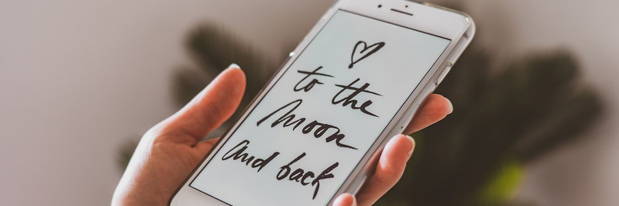 A person is holding a silver iPhone; the text on the screen reads 'To the moon and back'.